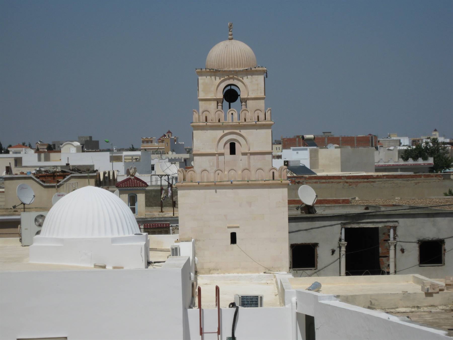 Stone minaret with dome rising above whitewashed medina rooftops in sunlight