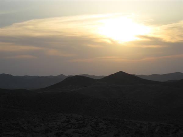 The sun behind clouds lights the dark ridges of the hills