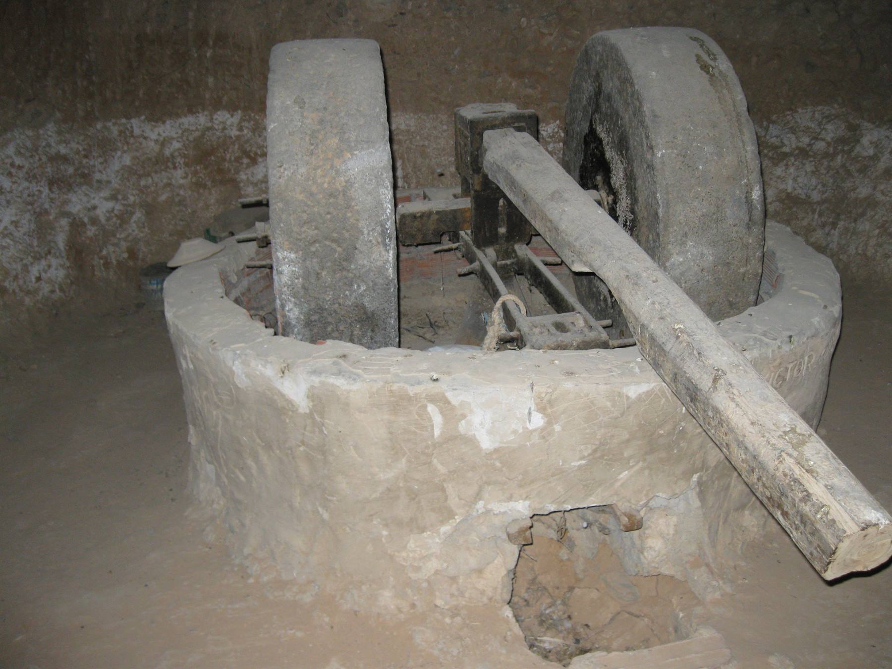 Ancient stone press with grinding wheels and wooden beam in dim light