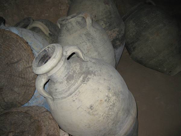 Clay amphorae with handles covered in dust, piled in a dark storeroom