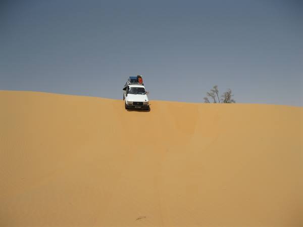 White off-road vehicle descending a sand dune, blue sky
