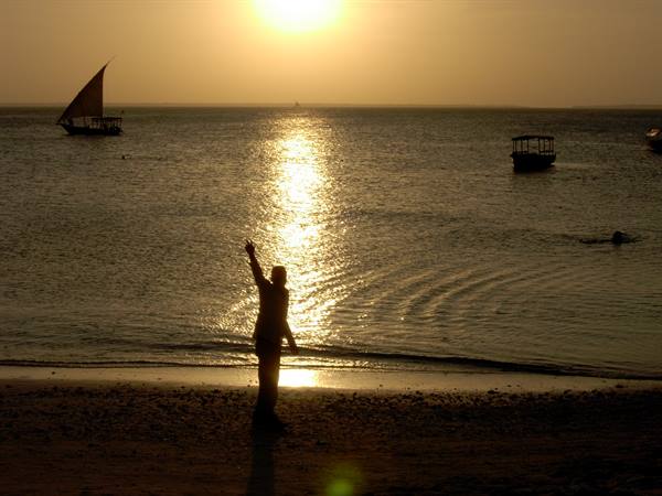 Silhouetted man waving on the beach, dhow and boats on golden sea