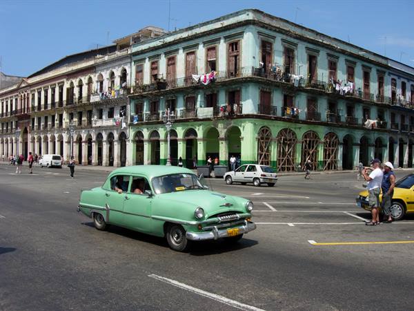 Vintage green car crossing the street by colonial building with balconies in Havana