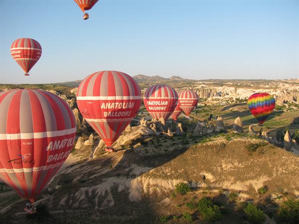 Red Anatolian hot air balloons drifting over Cappadocia's rock formations