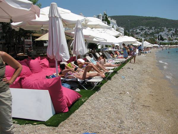 Sunbathers on loungers with pink cushions under white umbrellas, sandy beach
