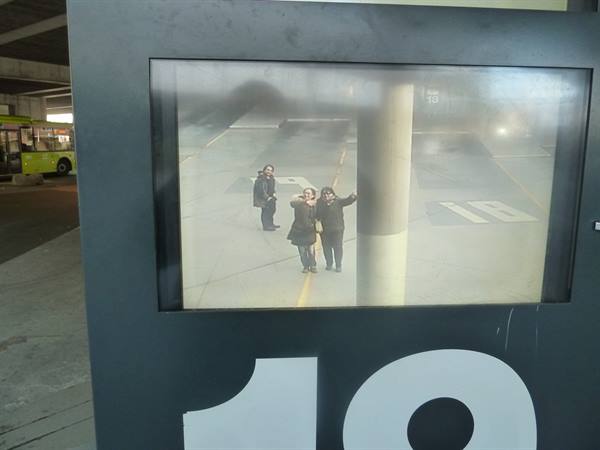 CCTV monitor at bus stop 19, travelers wave from the shelter