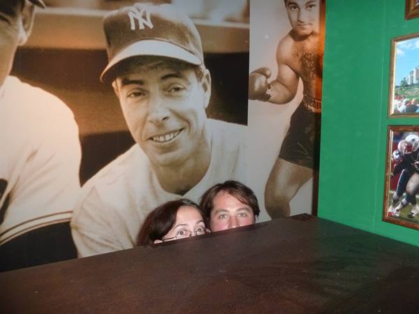 Couple peeks over wooden table in front of vintage sports photos