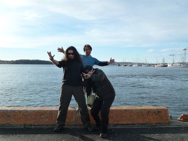 Three friends posing on Oslo harbor pier, boats and cranes behind them