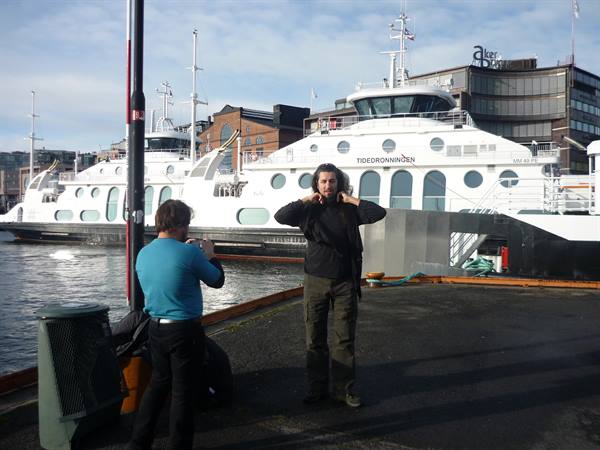 Tourist poses at Aker Brygge pier in front of ferry Tjødenronningen, Oslo