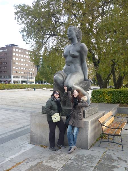 Two tourists posing beside a bronze female statue in an Oslo square