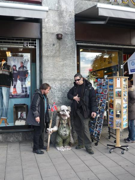 Two men posing beside a troll statue with a Norwegian flag outside Oslo shops