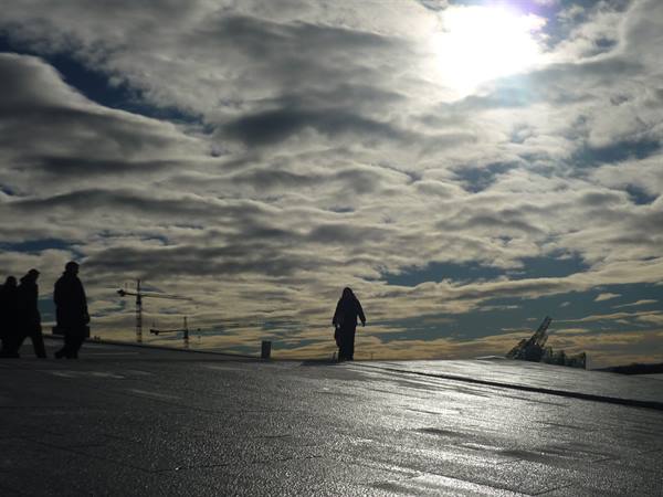 Visitors walk on the sloped marble roof of Oslo Opera House under clouds