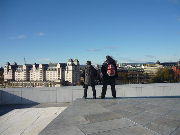 Two tourists on the sloped marble roof of Oslo Opera House overlooking the city