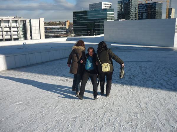Tourists walk on the snowy roof of Oslo Opera House, skyscrapers behind