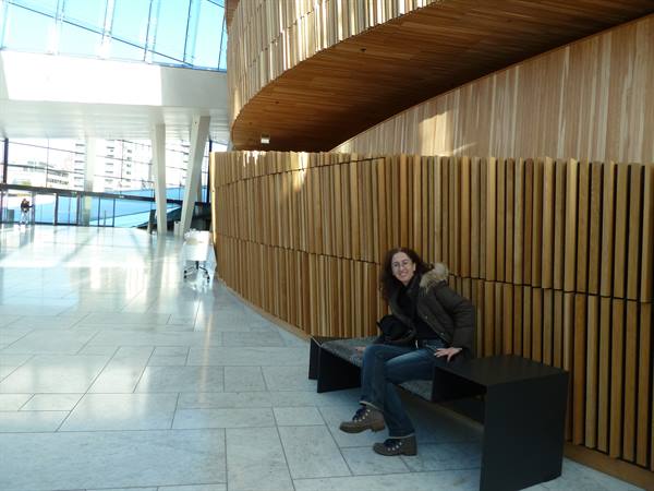 Woman sitting on a black bench inside Oslo Opera House, curved oak walls