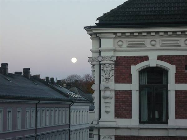 Brick and white stucco facades in Oslo, full moon in pale sky