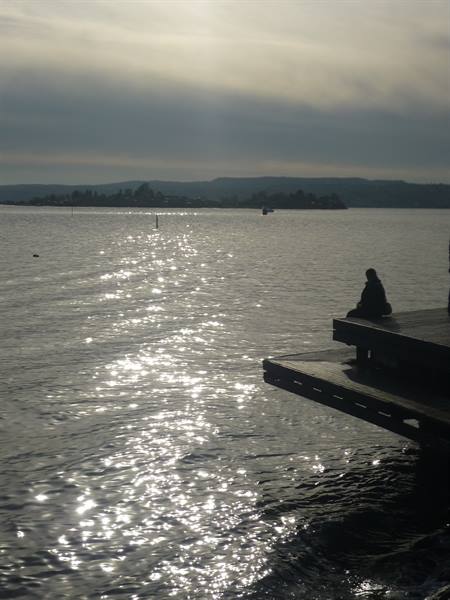 Person sitting on wooden pier by Oslofjord, sparkling water