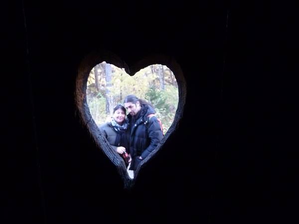 Couple framed through a heart carved in wood, autumn trees in background
