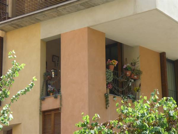 Facciata ocra con balconi pieni di fiori e piante rampicanti