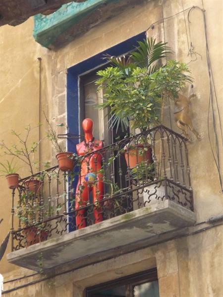 Red mannequin among potted plants on a wrought-iron balcony