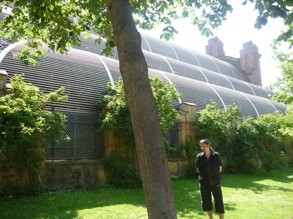 Woman standing on lawn beneath curved glass greenhouse roofs and brick walls