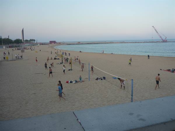 City beach with people playing beach volleyball on sand, evening light