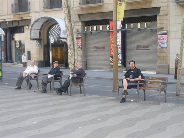 Men sitting on benches in front of shuttered Club Capitol, daylight