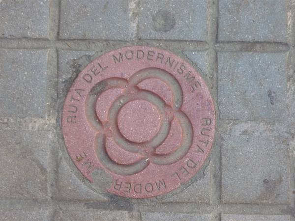 Round red Ruta del Modernisme plaque embedded in Barcelona sidewalk pavement
