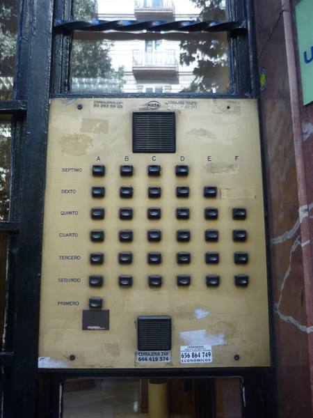 Worn brass intercom panel with six buttons per floor in a building lobby