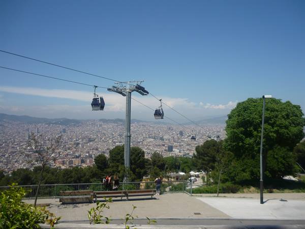 Cable cars gliding over Barcelona rooftops, benches and pines under blue sky