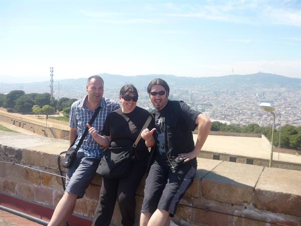 Three tourists smile leaning on a stone wall above Barcelona