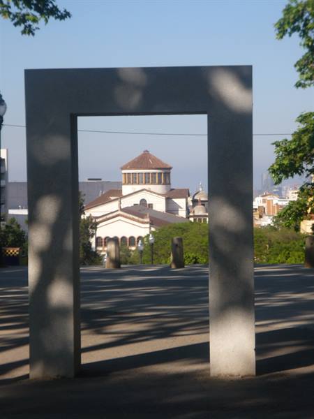 Concrete portal frames a domed church among green trees