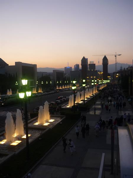 Walkway with illuminated fountains and green lampposts at dusk