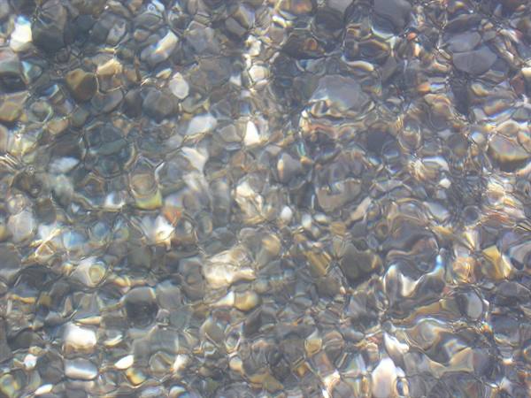 Gray and amber pebbles under clear water, shimmering light reflections