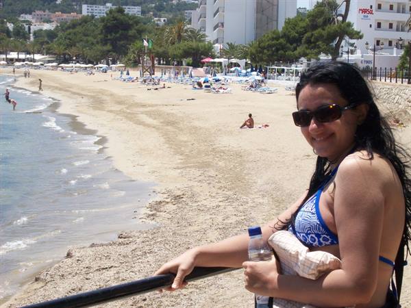 Smiling woman in blue bikini on crowded beach with umbrellas and swimmers