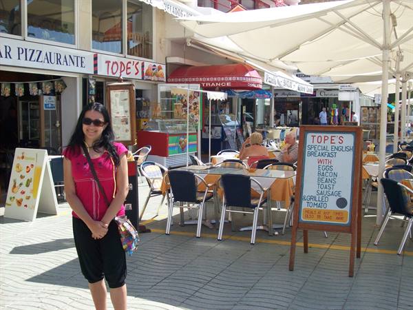 Smiling woman outside Topé's pizzeria, parasols and tables on the promenade
