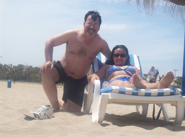 Man in black swimwear beside woman on striped beach lounger under sunny sky