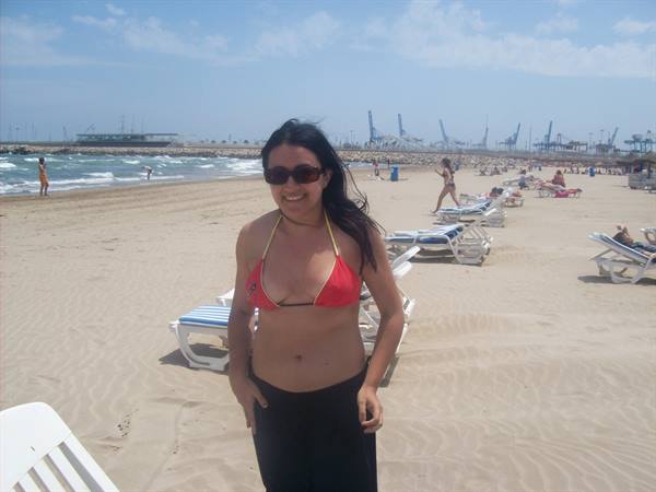 Smiling woman in red bikini on sand, sunbeds and port cranes behind
