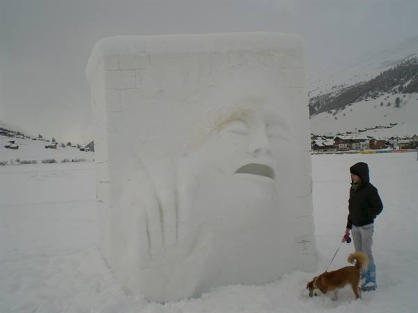 Woman with dog beside a snow sculpture of a face, snowy mountain