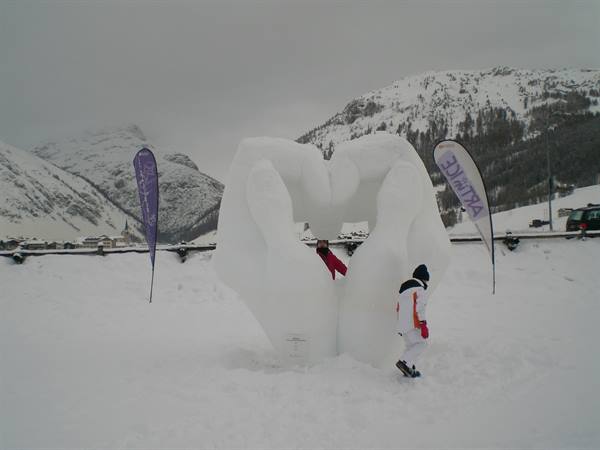 Snow sculpture of hands forming a heart, child nearby, snowy mountains