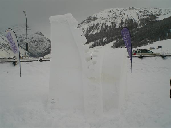 Snow sculpture with flags, snowy mountains and a car in the background