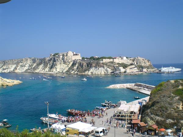 Tremiti Islands harbor with ferry, tourists, and San Nicola monastery on cliff