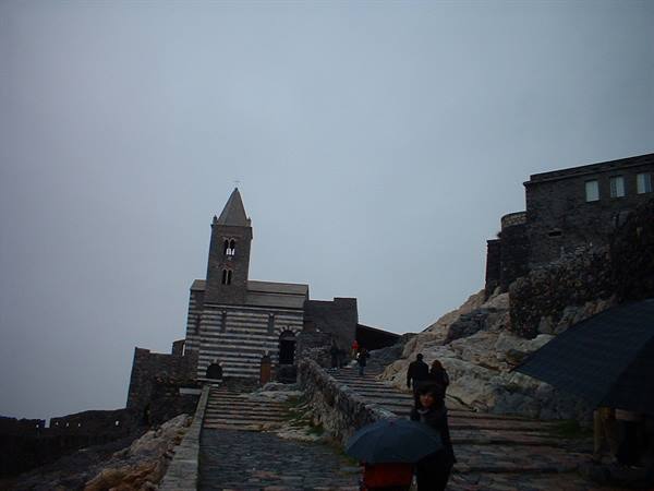 Tourists with umbrella climb the stone staircase toward San Pietro church in Portovenere