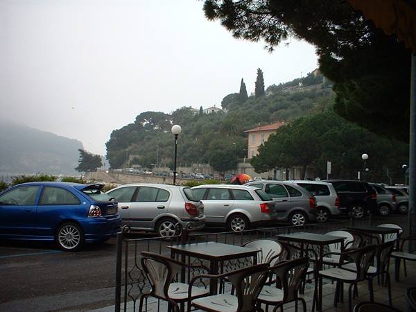 Parked cars in front of an iron café terrace by a foggy seafront