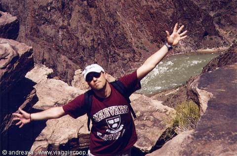 Man with outstretched arms on Grand Canyon rocks, green Colorado River below