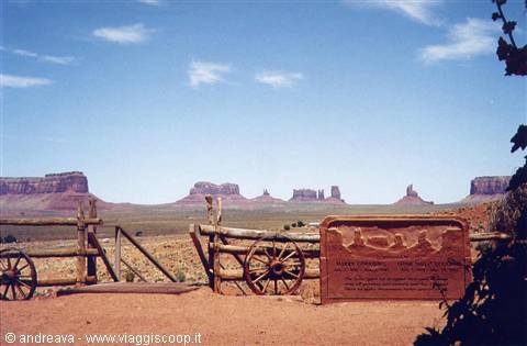 Wooden sign and wagon wheels before the buttes of Monument Valley