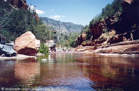 People wading in Oak Creek amid red rocks and mountains