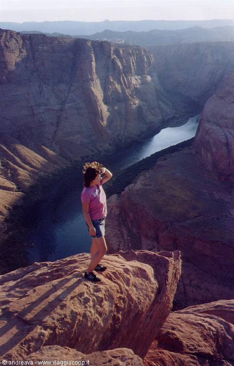 Girl standing on rock above Horseshoe Bend, the Colorado winding below