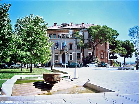 sunny town square with fountain, historic building with flags, trees and parked cars