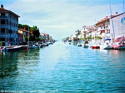 Boats moored along the Grado canal between colorful houses